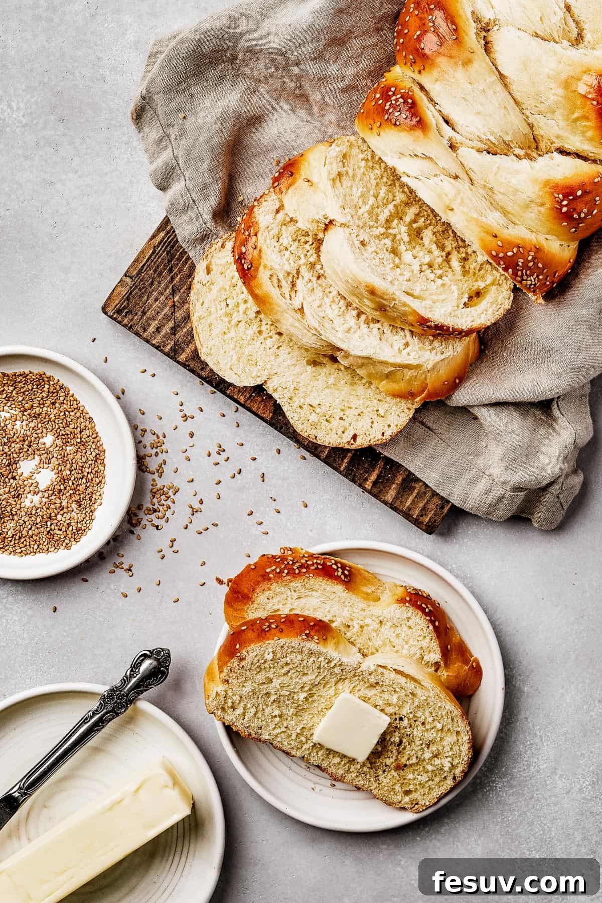 Golden Braids of Challah Perfection 11 An inviting overhead shot of a rustic wooden cutting board draped with a tea towel, displaying perfectly sliced braided challah bread arranged artfully.