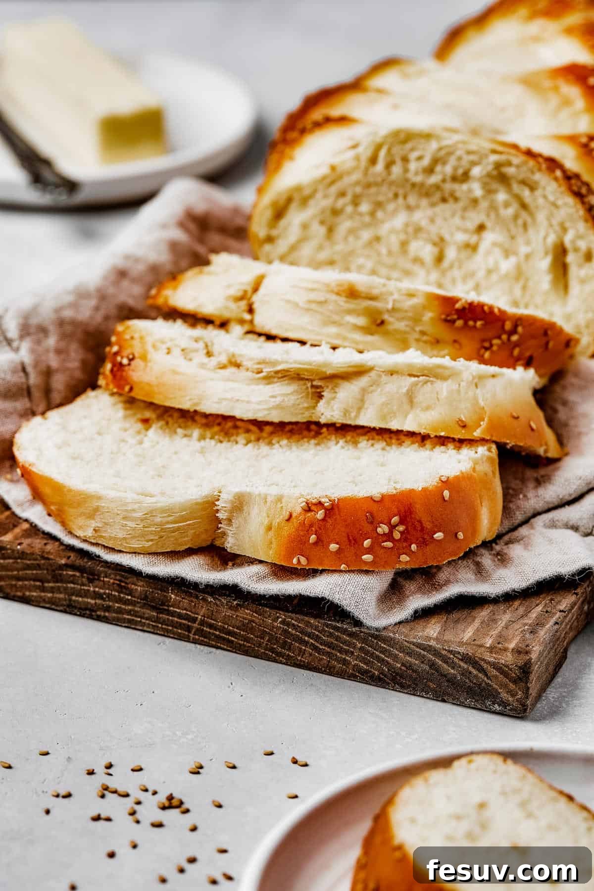 Golden Braids of Challah Perfection 4 A charming wooden cutting board adorned with a patterned tea towel, presenting slices of a beautifully braided challah bread, ready for serving.
