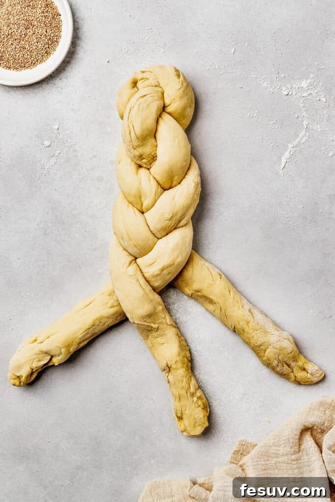 Golden Braids of Challah Perfection 7 Three long pieces of challah dough being skillfully braided together on a wooden surface, showcasing the beginning of the bread's iconic shape.