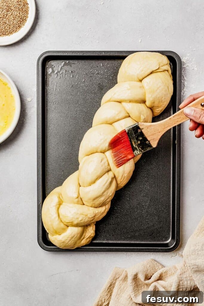 Golden Braids of Challah Perfection 8 An unbaked challah loaf, gracefully braided, resting on a sheet pan, being meticulously brushed with a golden egg wash, preparing it for a perfect crust.