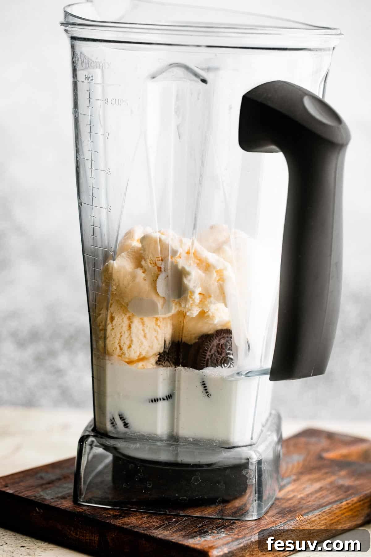 The inside of a blender jar, partially filled with creamy vanilla ice cream, whole milk, heavy cream, and several dark Oreo cookies, ready to be blended into a delicious frozen treat.