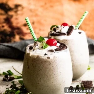 Two drinking glasses filled with Shamrock Oreo McFlurry Shake, topped with whipped cream, maraschino cherries, and mint leaves.