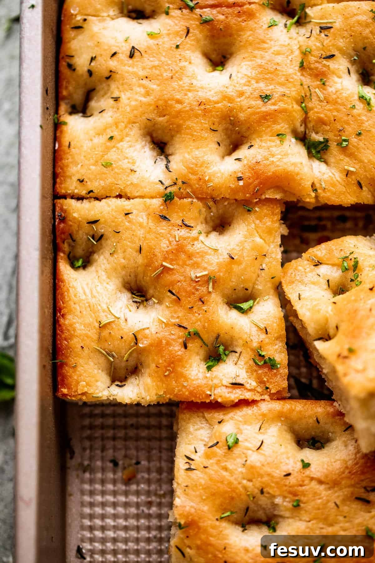 Pillowy Herb-Kissed Garlic Focaccia 3 A large pan-sized loaf of focaccia, with one corner neatly cut away, highlighting its perfectly golden crust and tender interior.