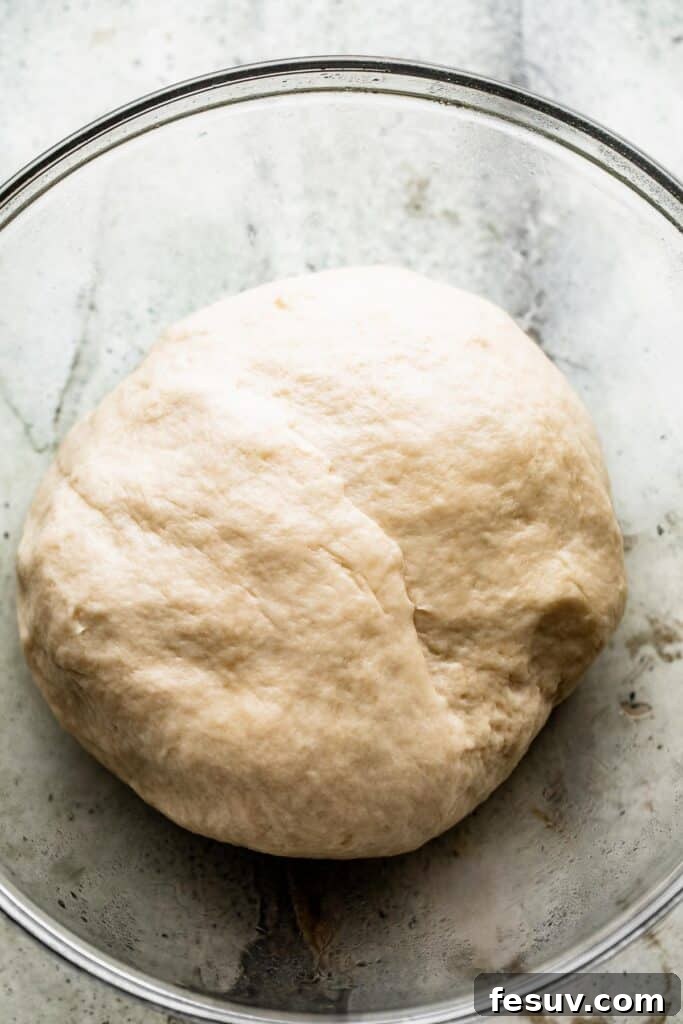Pillowy Herb-Kissed Garlic Focaccia 5 A glass bowl containing a perfectly risen, smooth ball of bread dough, coated lightly with olive oil.