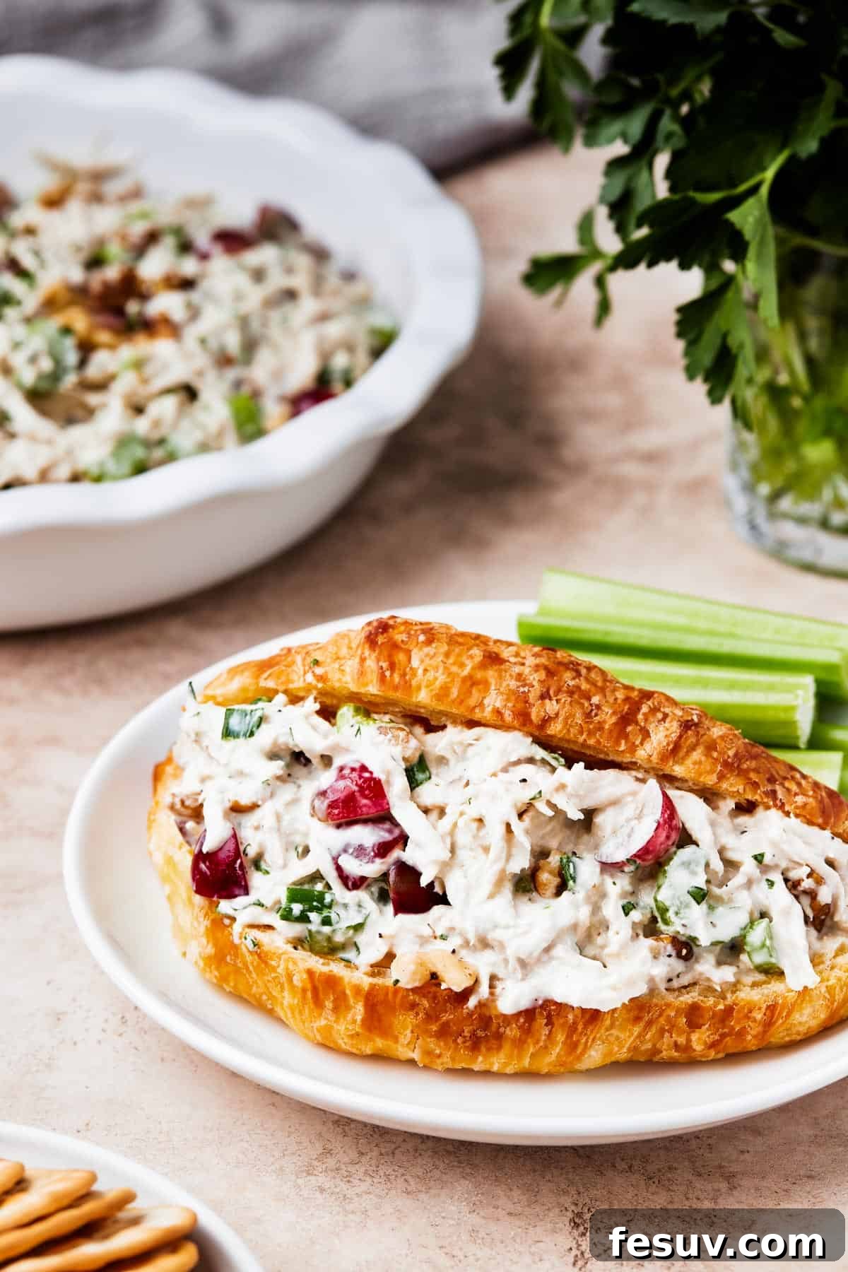 Close-up of chicken salad served in a split croissant, garnished with fresh herbs.