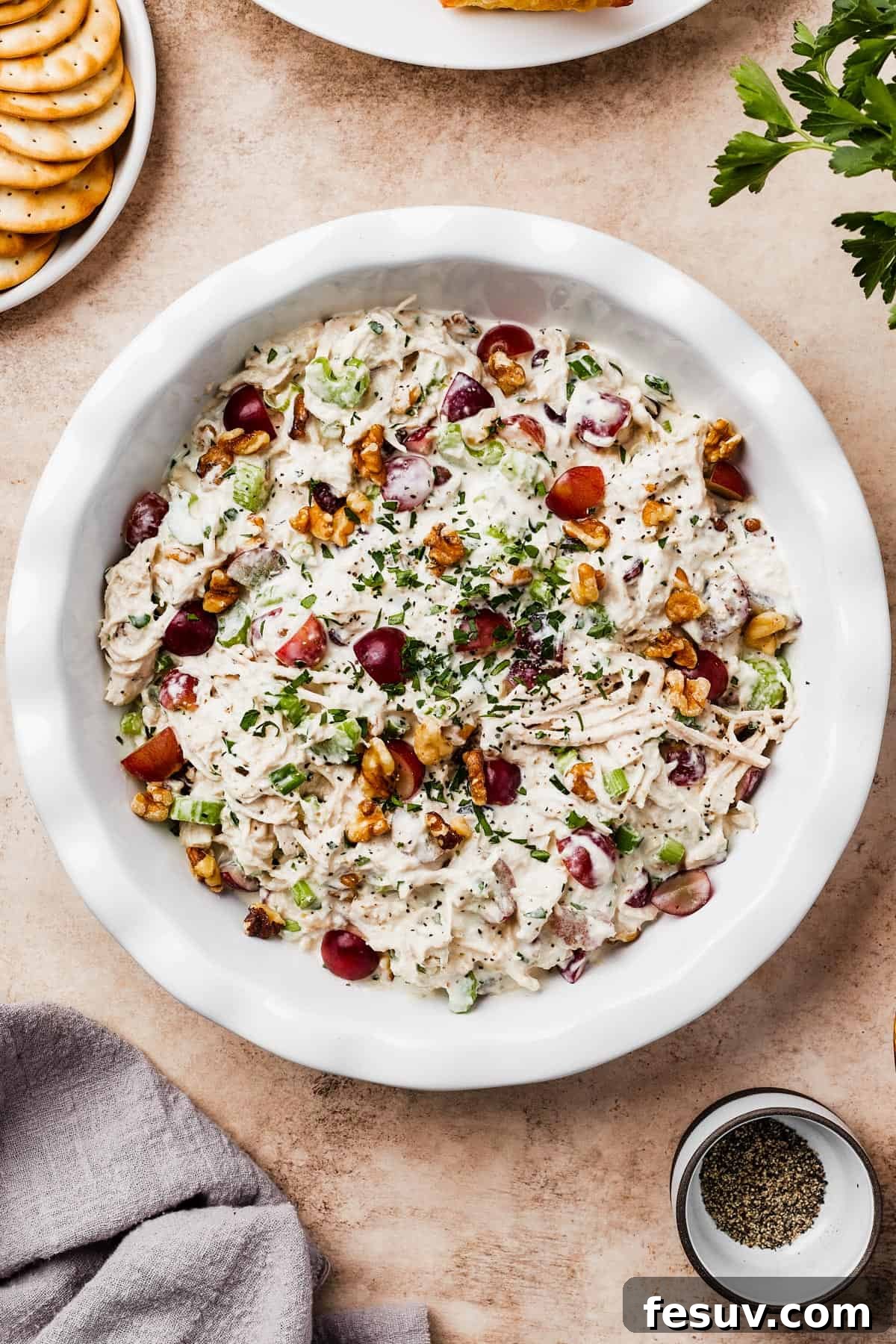 A shallow white dish filled with creamy chicken salad, garnished with nuts and fresh herbs.
