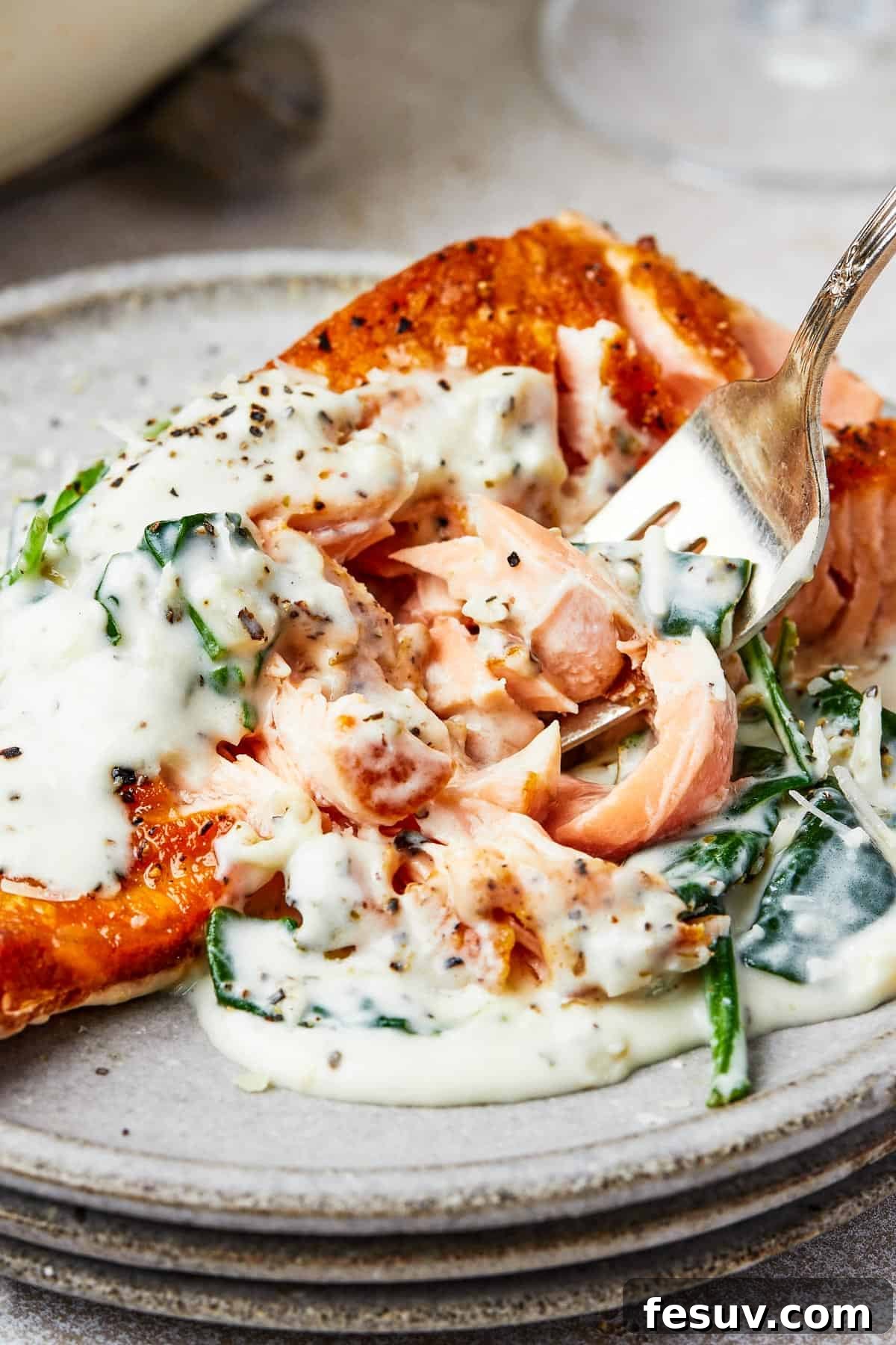 A serving of salmon Florentine, with a fork lifting a bite towards the camera, showcasing the creamy sauce and tender fish.