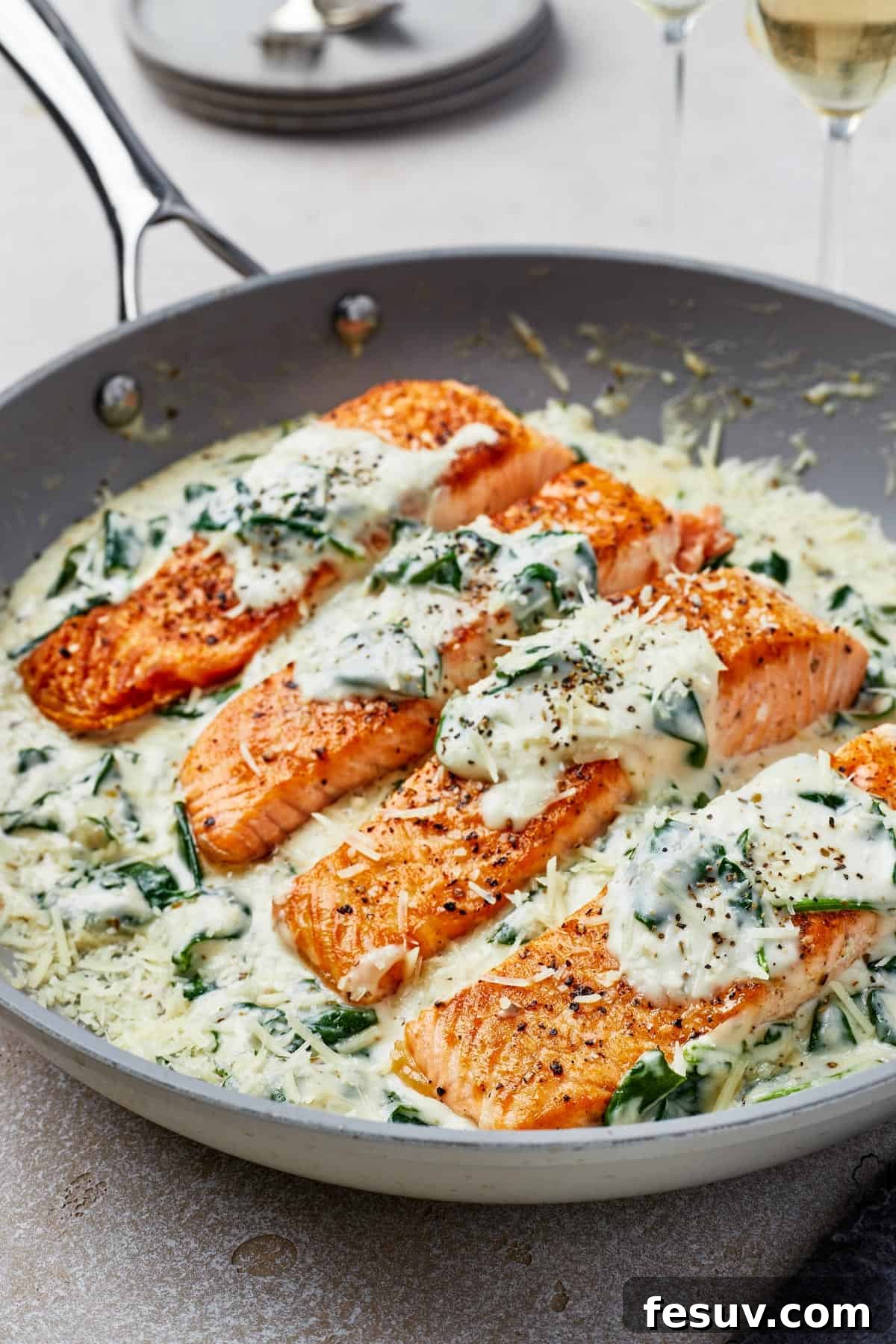 Close-up shot of perfectly pan-fried salmon fillets immersed in the rich Florentine sauce, flecked with spinach.