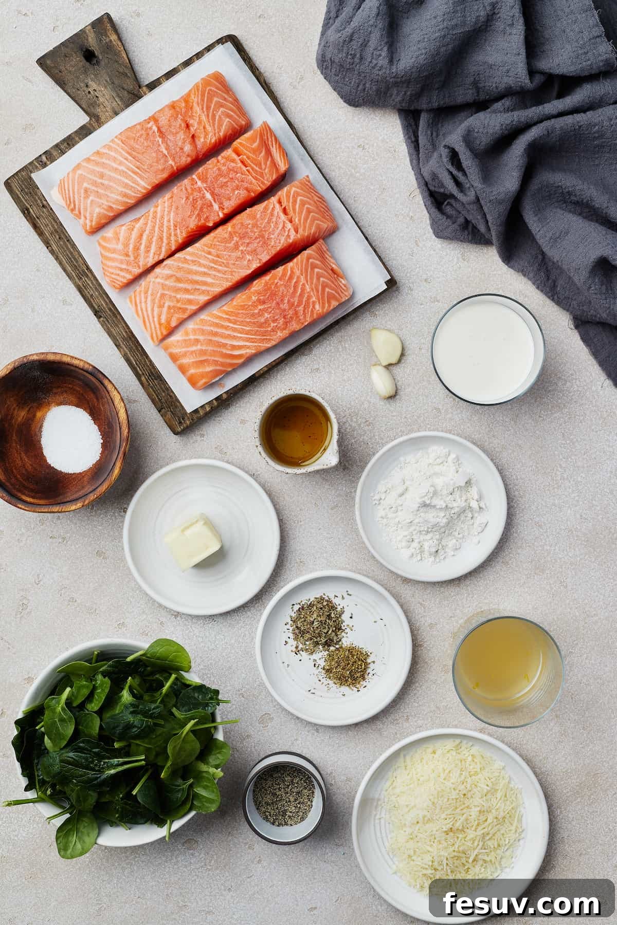 Ingredients laid out for Salmon Florentine: salmon fillets, garlic, heavy cream, salt, butter, olive oil, flour, dried herbs, chicken broth, spinach, pepper, Parmesan cheese