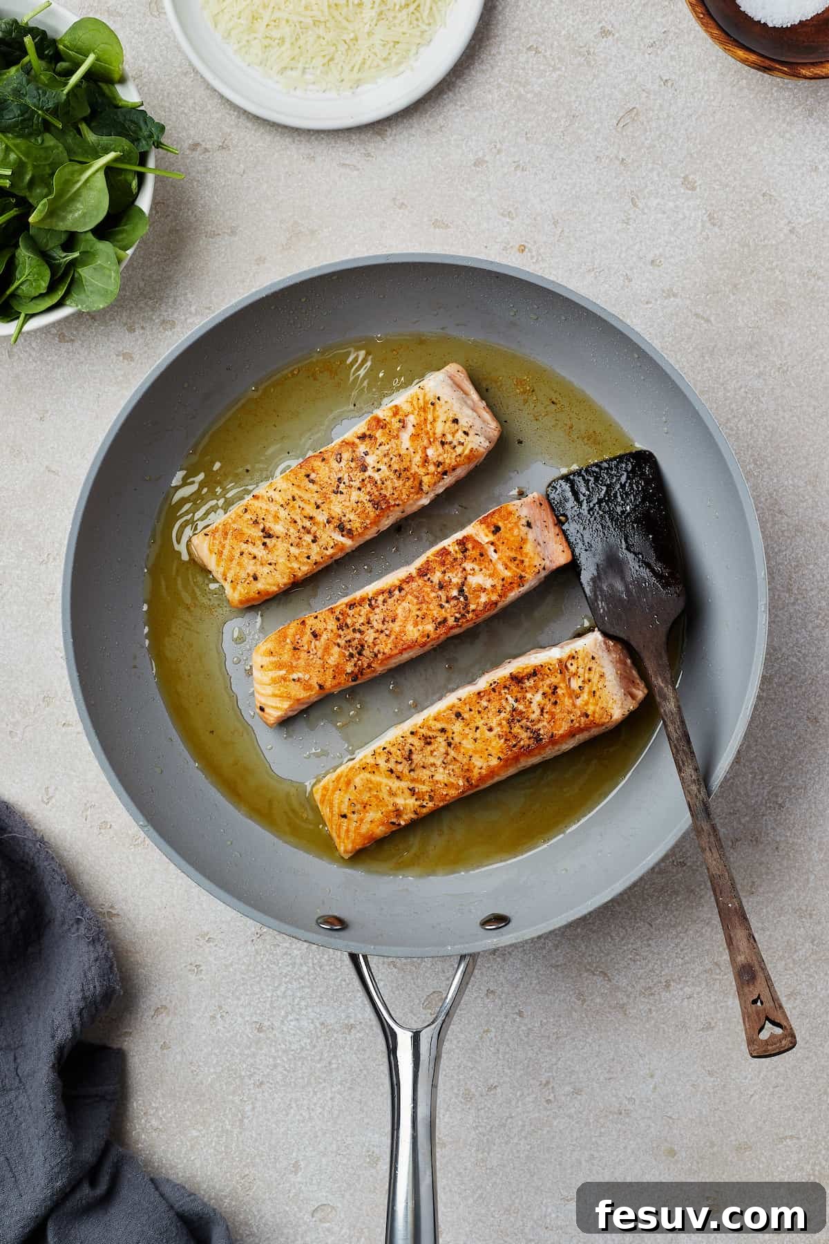 Salmon fillets cooking in a skillet, getting a golden-brown sear.