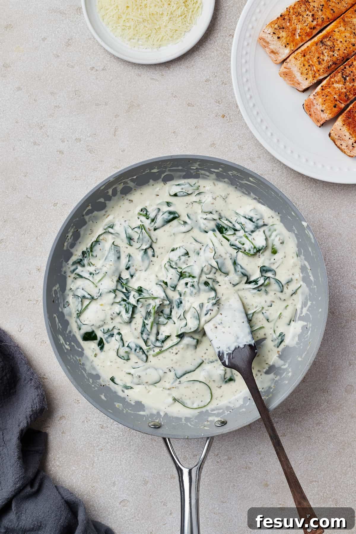 A creamy spinach sauce simmering in a nonstick skillet, ready for the salmon.