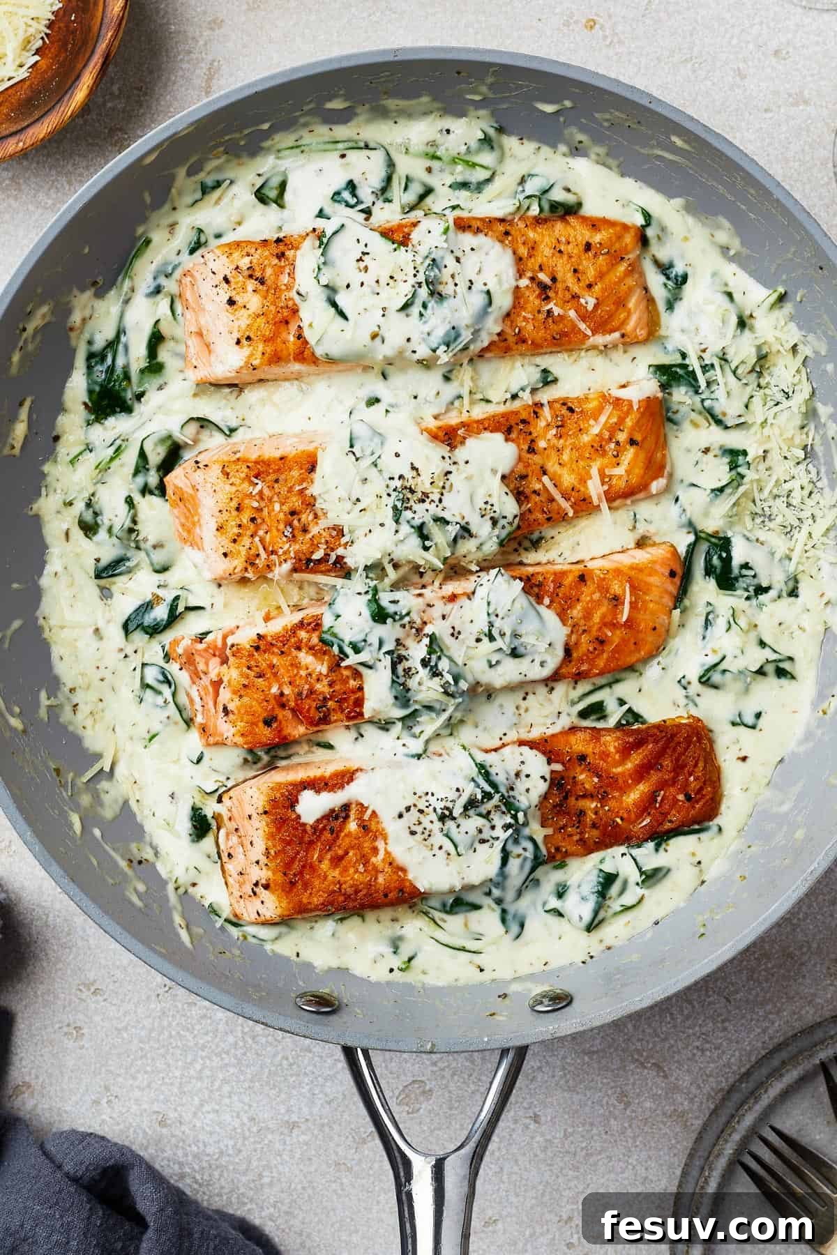 Salmon fillets in creamy spinach sauce presented in a gray nonstick skillet, ready to be served.