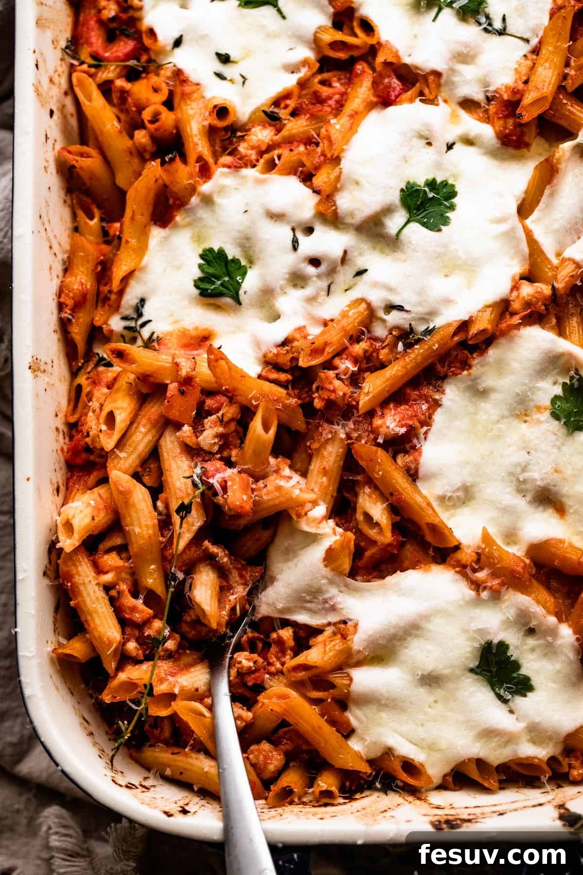 Velvet Penne Vodka Bake 2 An inviting overhead shot of a baking dish filled with golden-brown Baked Penne Alla Vodka, generously topped with glistening melted mozzarella cheese and fresh basil garnish, ready to be served.