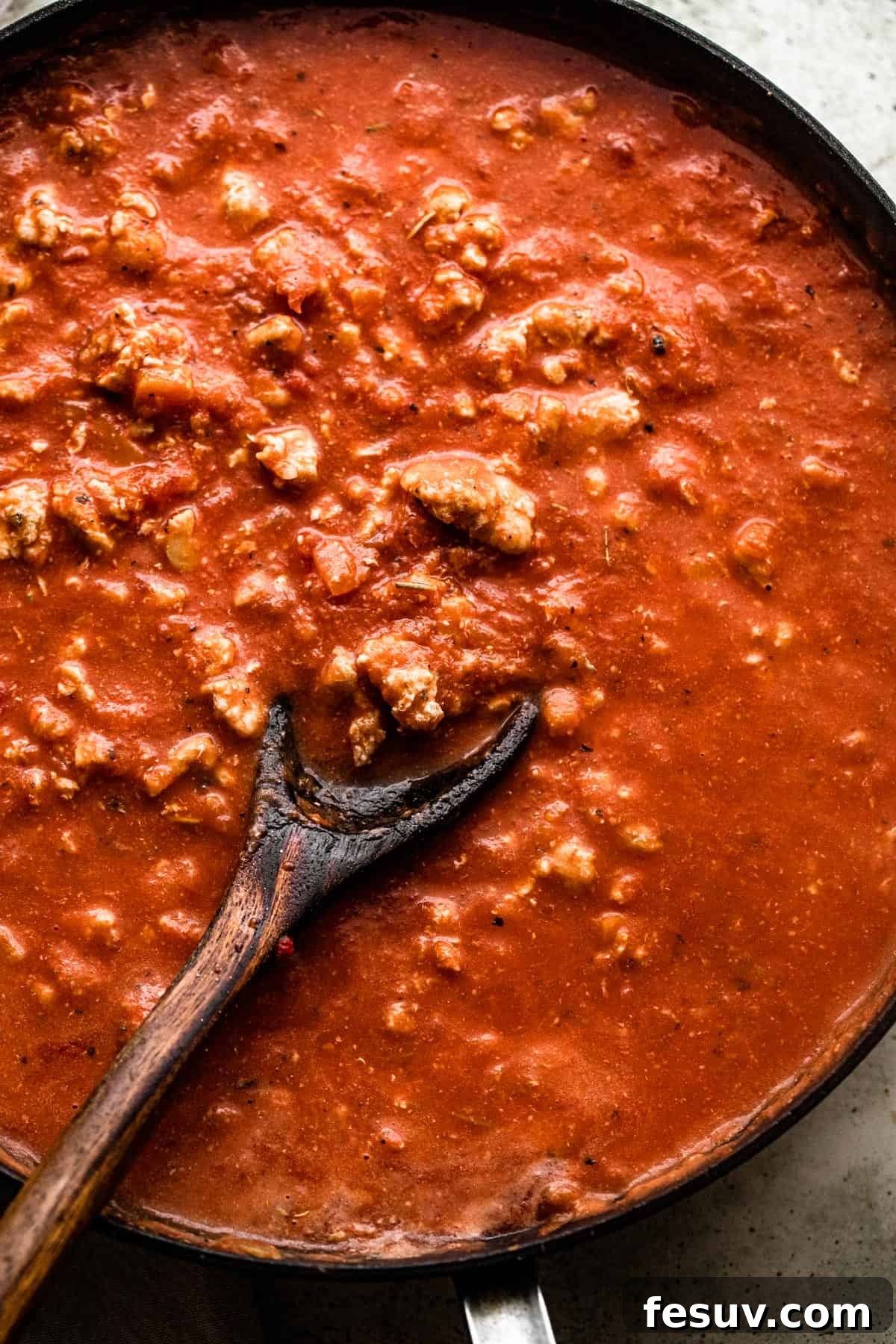 Velvet Penne Vodka Bake 4 A wooden spoon actively stirring savory ground turkey into a rich, simmering tomato sauce within a large skillet, creating the flavorful base for the baked penne.