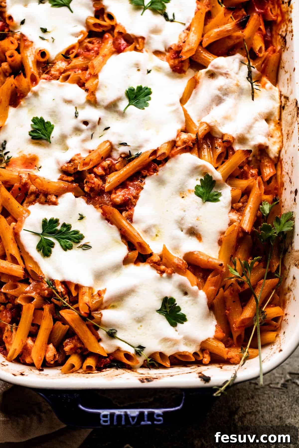 Velvet Penne Vodka Bake 6 A close-up overhead shot of a baking dish filled with Baked Penne Alla Vodka, featuring a golden-brown, bubbly layer of melted mozzarella cheese and tender penne pasta within the rich, creamy sauce.