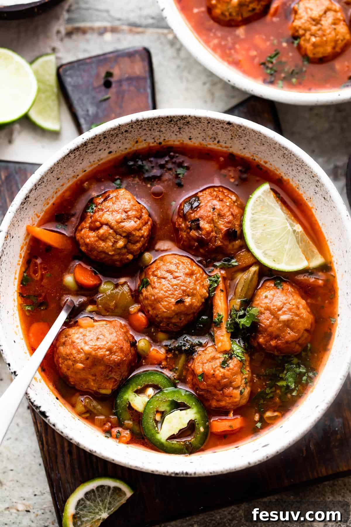 Hearty Mexican Meatball Soup 2 overhead shot of two soup bowls filled with albondigas soup and garnished with limes and sliced jalapenos.