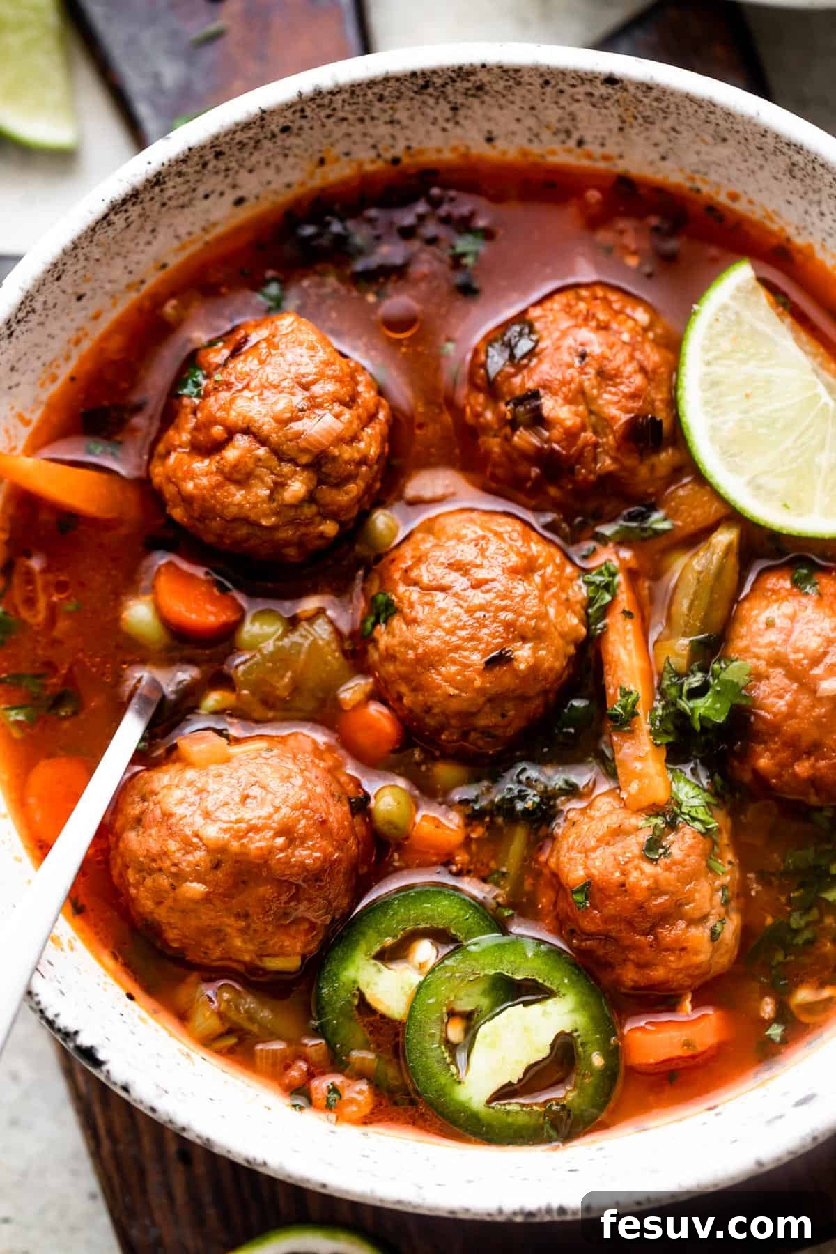 Hearty Mexican Meatball Soup 3 close up overhead shot of soup bowl filled with albondigas soup and garnished with limes and sliced jalapenos.
