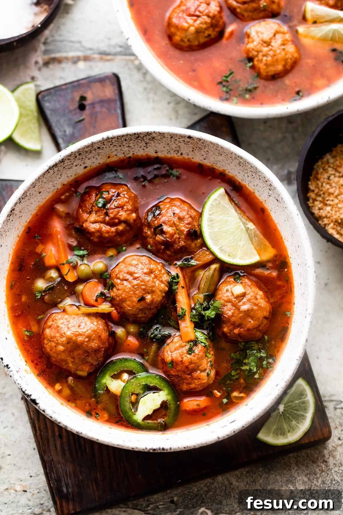 Hearty Mexican Meatball Soup 6 overhead shot of two soup bowls filled with albondigas soup and garnished with limes and sliced jalapenos.