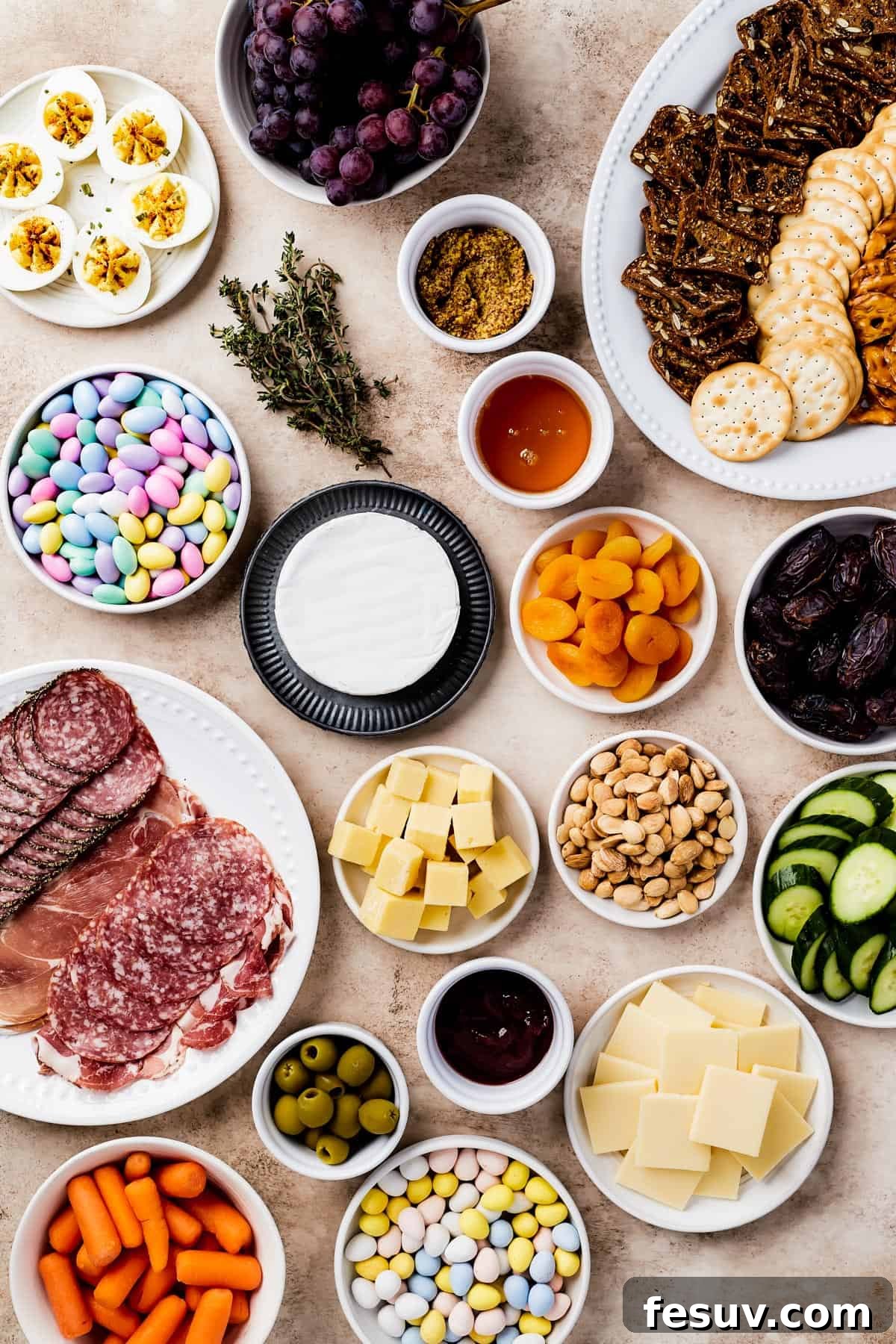 Craft the Perfect Easter Charcuterie Board 4 An overhead shot of a complete Easter charcuterie board featuring deviled eggs, red grapes, a platter of assorted crackers, vibrant Jordan almonds, fresh thyme sprigs, hearty grainy mustard, sweet strawberry preserves, a creamy wheel of brie, chewy dried apricots, rich Medjool dates, a selection of sliced cured meats, cubed white cheddar, crunchy Marcona almonds, refreshing sliced cucumber, briny Castelvetrano olives, golden honey, and smooth gouda cheese.