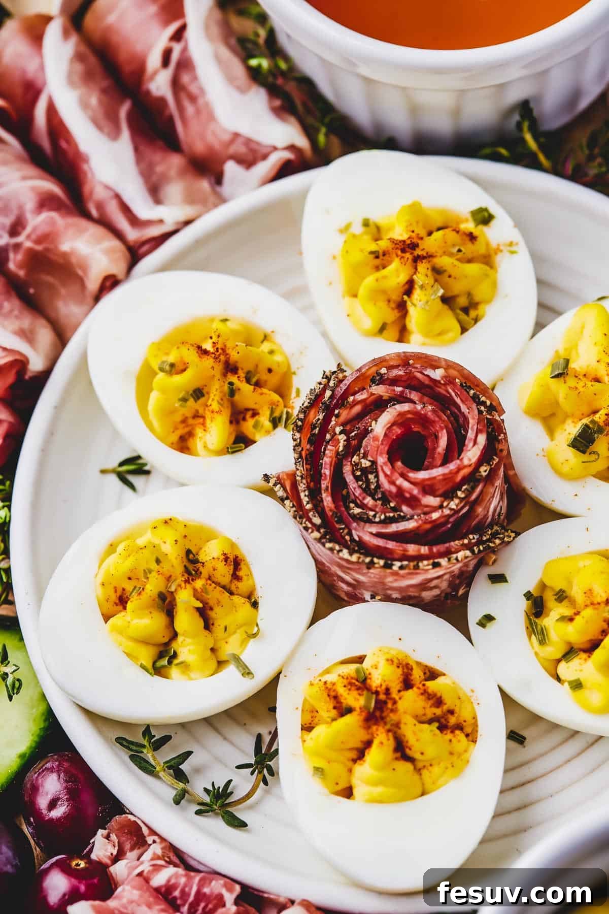 Craft the Perfect Easter Charcuterie Board 8 A close-up shot of a plate of perfectly prepared deviled eggs, artfully garnished with a delicately folded slice of coppa in the center, embodying a sophisticated touch for an Easter charcuterie board.