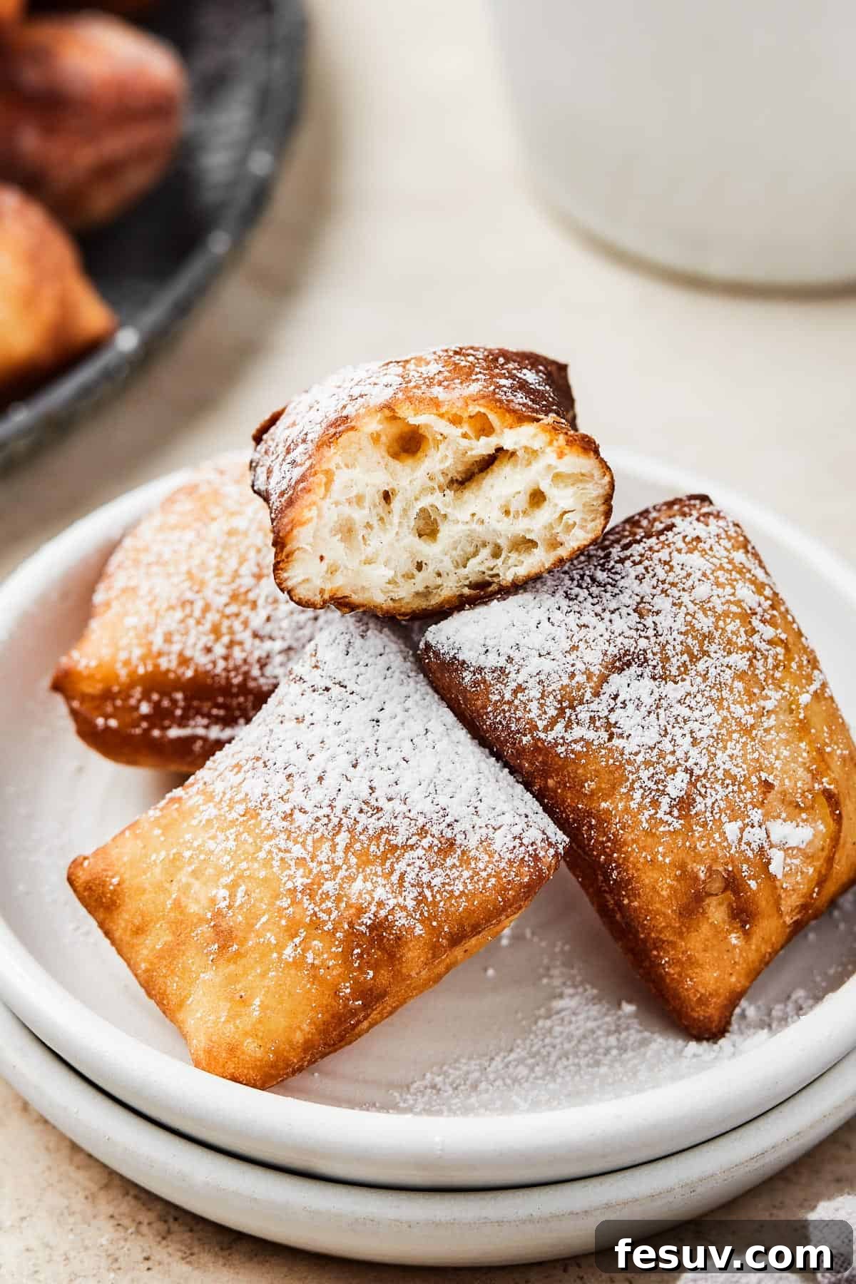 French Quarter Powdery Delights 11 Homemade square donuts on a plate. One has been broken in half to show the fluffy texture of the interior.