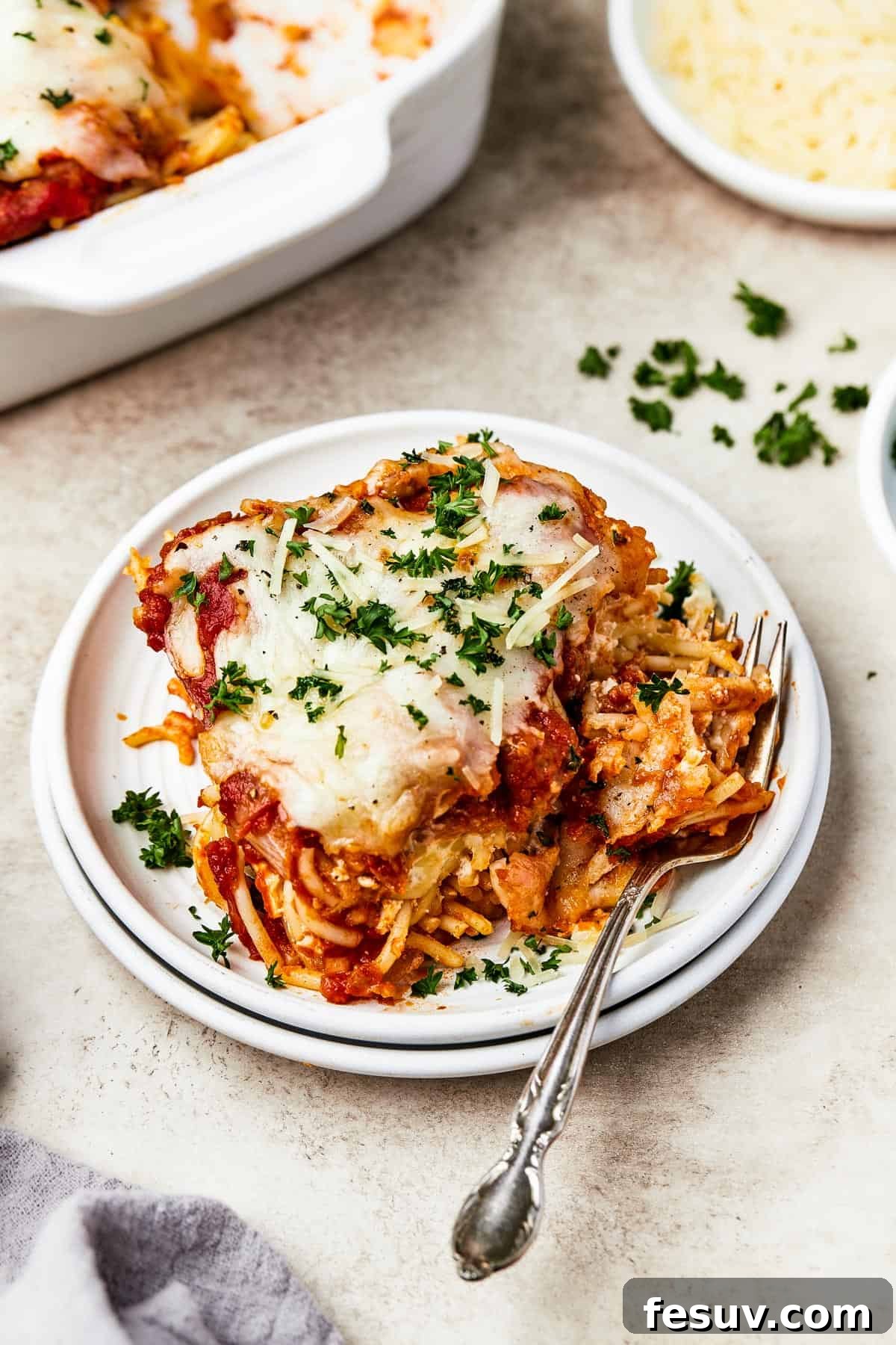 Irresistible Baked Spaghetti Delight 11 A square portion of baked spaghetti casserole on a white plate, garnished with fresh chopped parsley, highlighting its delicious layers.