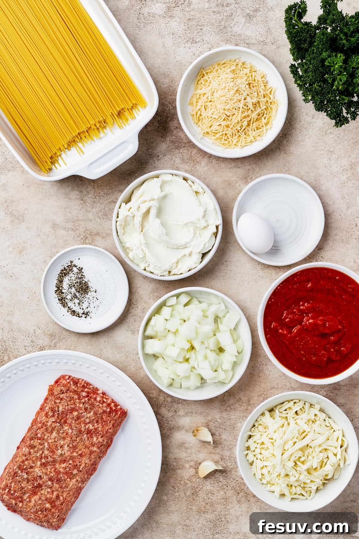 Irresistible Baked Spaghetti Delight 4 A flat lay photograph showcasing all the key ingredients for baked spaghetti casserole: dry spaghetti, yellow onion, various seasonings, creamy ricotta, an egg, shredded mozzarella, rich marinara sauce, Italian sausage, minced garlic, and grated parmesan cheese.