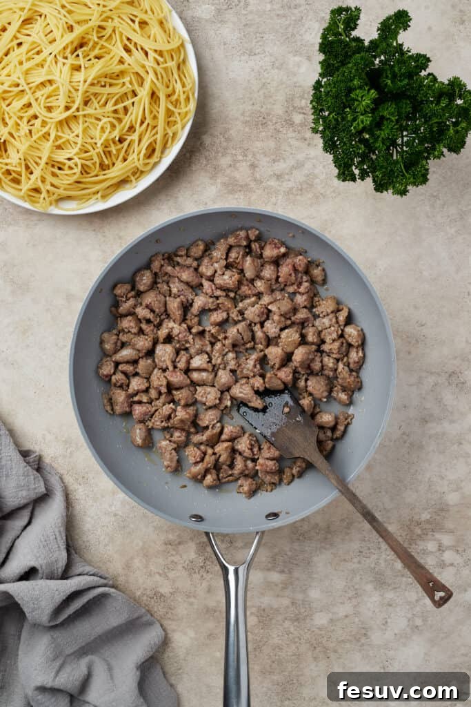 Irresistible Baked Spaghetti Delight 6 Crumbled Italian sausage browning in a large skillet, releasing savory aromas.