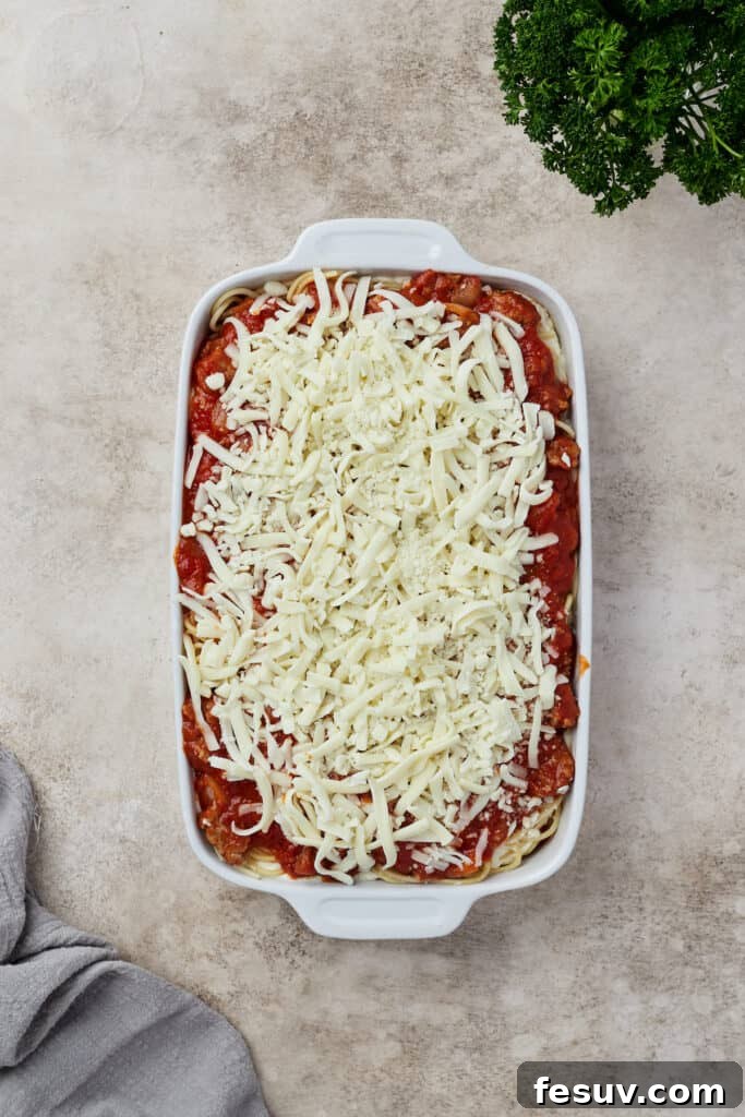 Irresistible Baked Spaghetti Delight 9 An unbaked spaghetti casserole, beautifully layered with sauce, pasta, ricotta, and topped with mozzarella and parmesan cheese, in a baking dish.