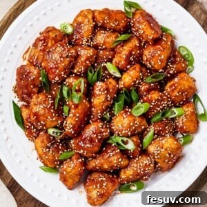 overhead shot of sweet and sour chicken served on a white plate with rice, green onions, and toasted sesame seeds, ready to be enjoyed.