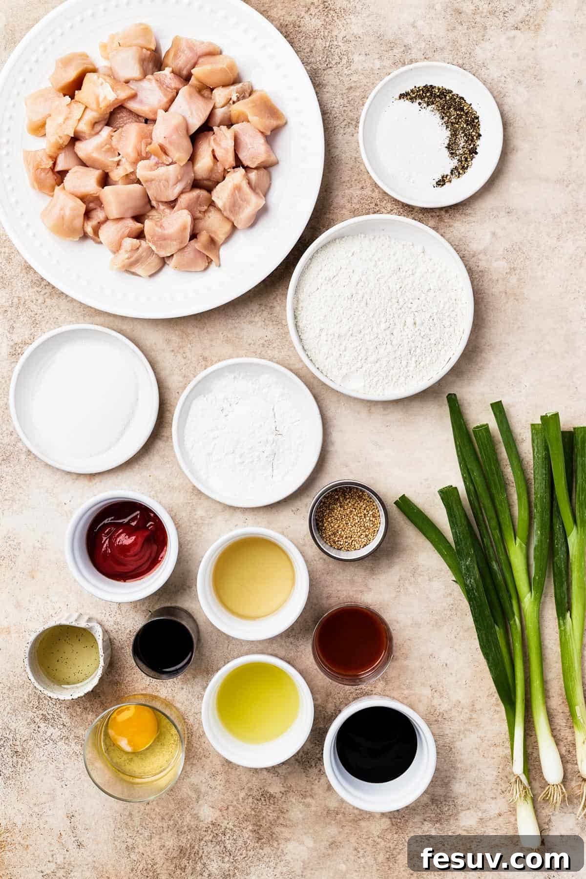 A vibrant flat lay of all ingredients for sweet and sour chicken: chicken breast, salt, pepper, sugar, cornstarch, flour, ketchup, oil, toasted sesame seeds, rice vinegar, oyster sauce, sriracha, egg, pineapple juice, soy sauce, and green onions.