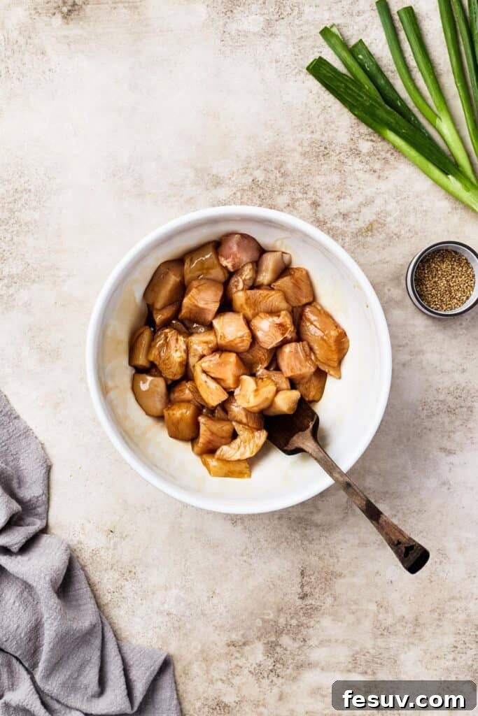 Chicken marinating in soy sauce in a white bowl, the first step in preparing homemade sweet and sour chicken.