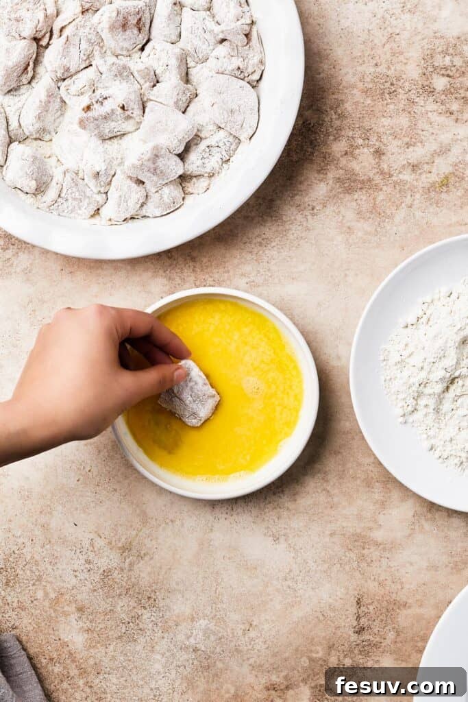 A well-organized chicken breading station with breaded chicken pieces, egg wash, flour mixture, and raw floured chicken on a plate, illustrating the double-breading process.