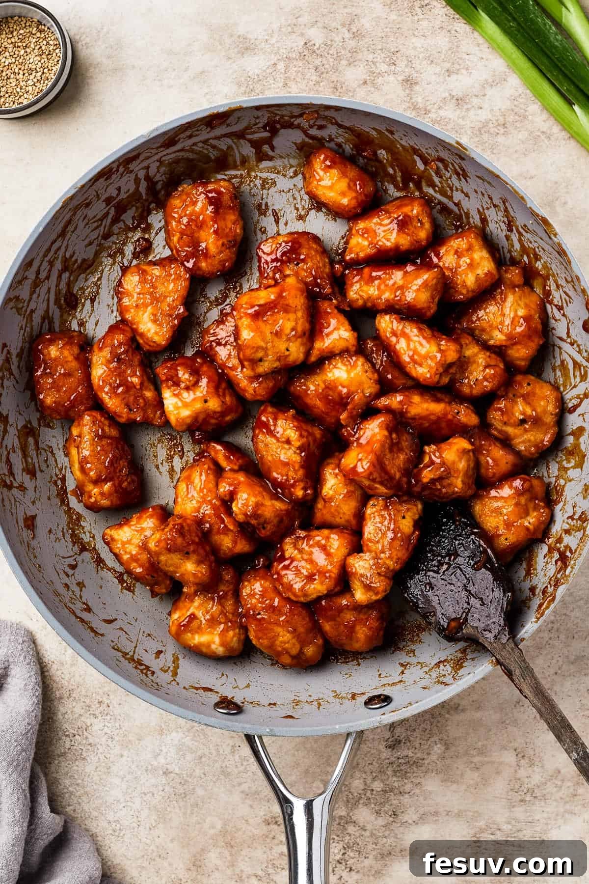 A close-up of a skillet full of perfectly fried chicken in a rich, glossy sweet and sour sauce, ready to be served.
