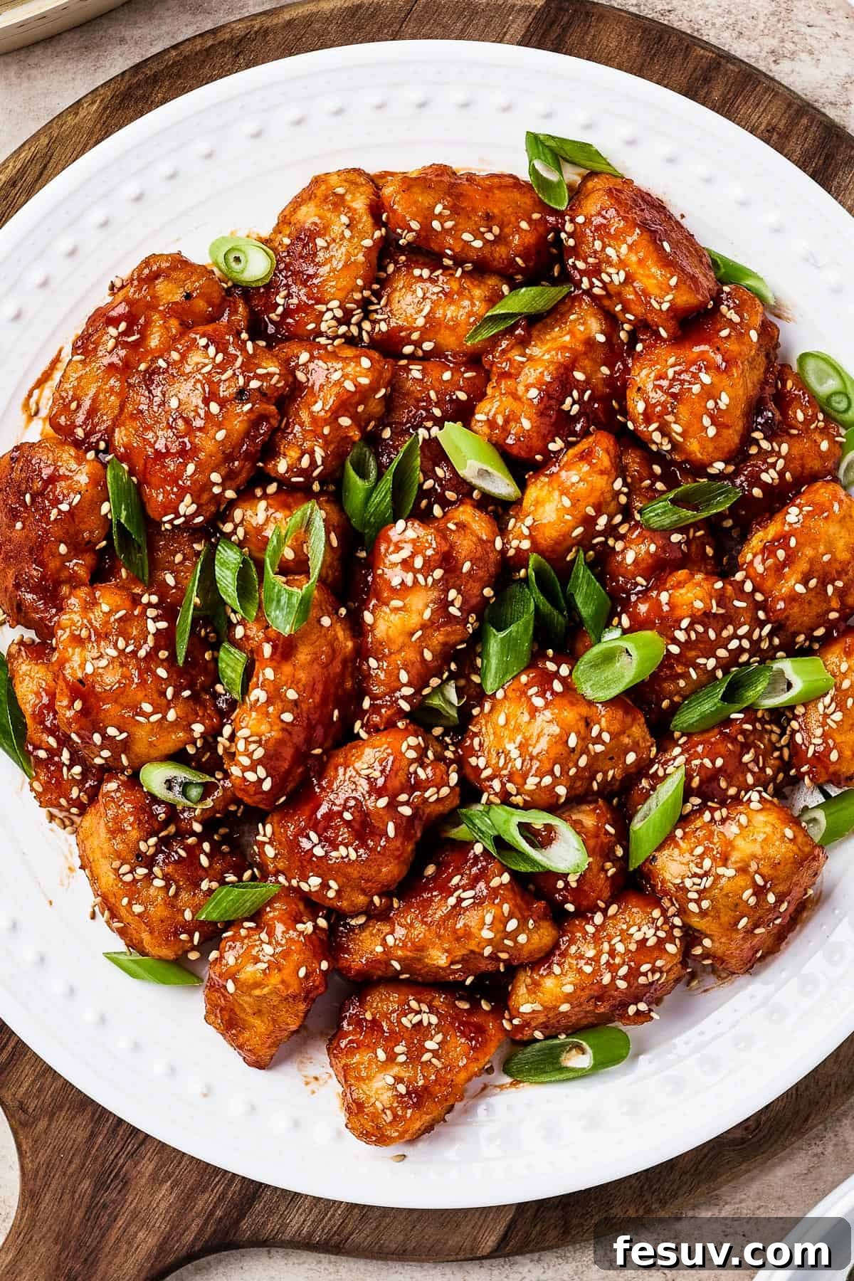 Close-up shot of crispy sweet and sour chicken pieces, garnished with green onions and toasted sesame seeds, served with white rice, showcasing the vibrant colors and appealing texture.