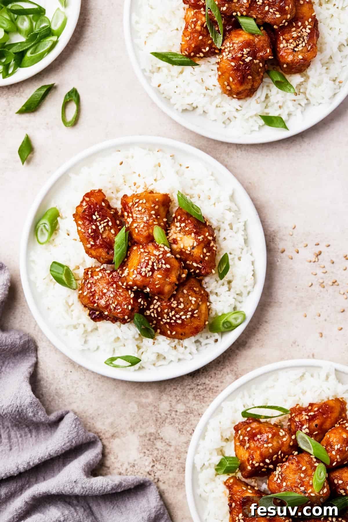 Three plates topped with fluffy white rice and generous portions of saucy, crispy sweet and sour chicken chunks, garnished with green onions.