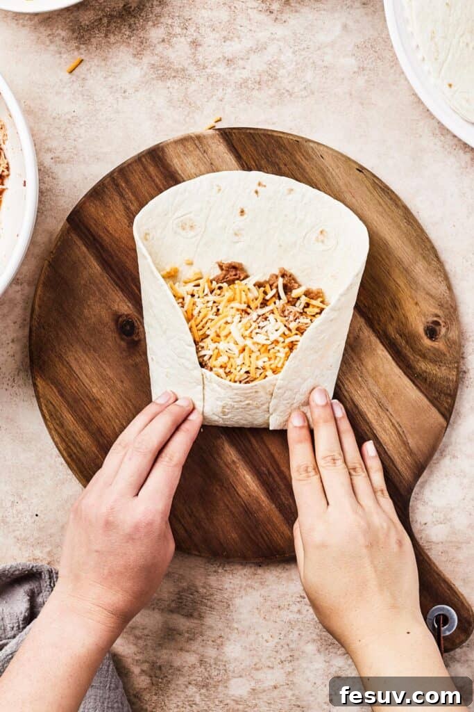 A woman folds the bottom and sides of a tortilla over the filling in the center of the tortilla.