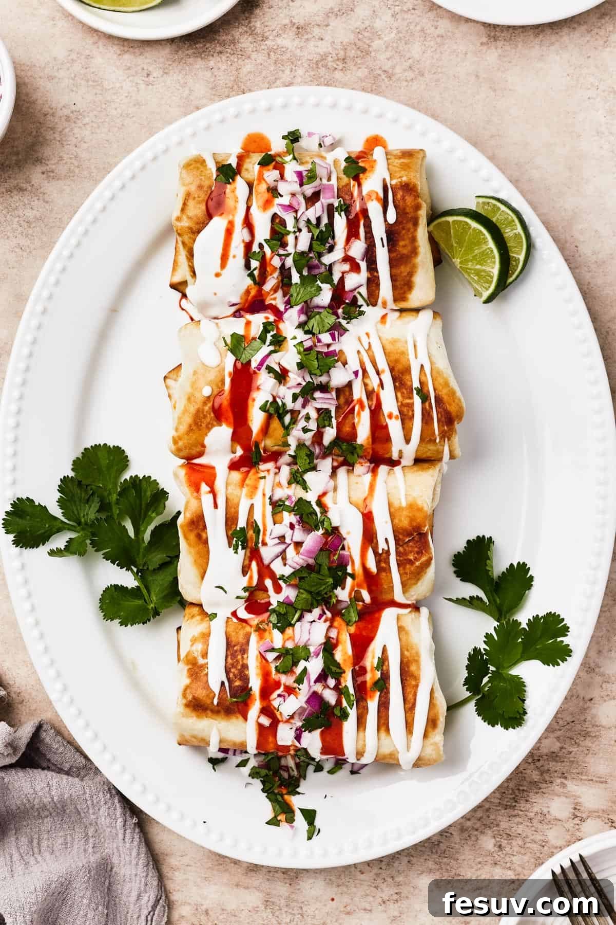 A plate of fried chimichangas, garnished with sour cream, hot sauce, cilantro, lime, and chopped red onion.