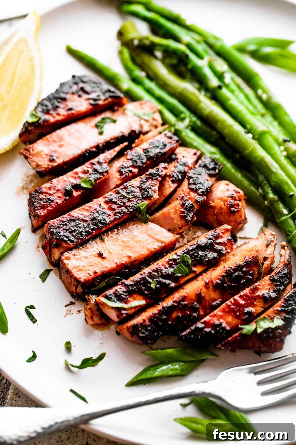 Overhead close-up shot of perfectly sliced blackened balsamic tuna served on a white dinner plate with vibrant green asparagus stalks.