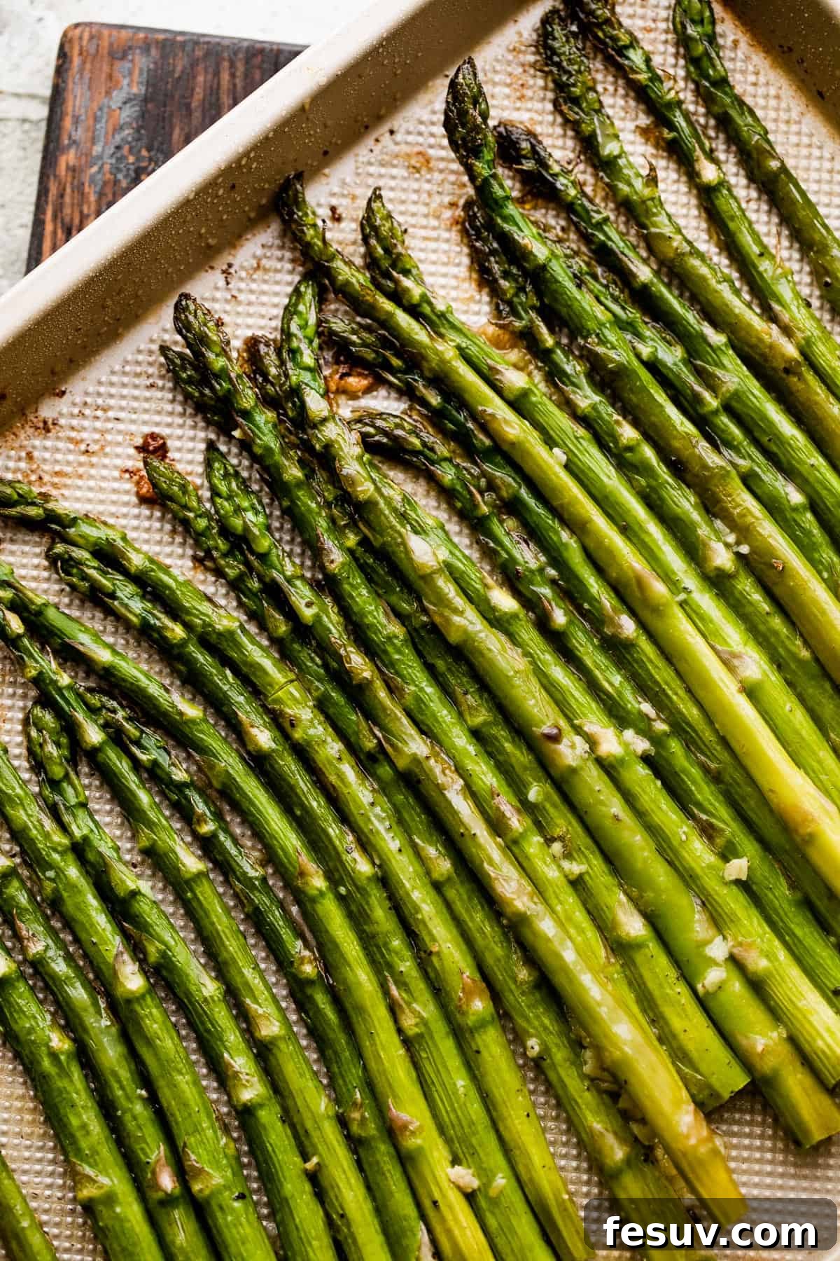 Fresh asparagus spears arranged neatly on a gold-colored baking sheet, ready for roasting.