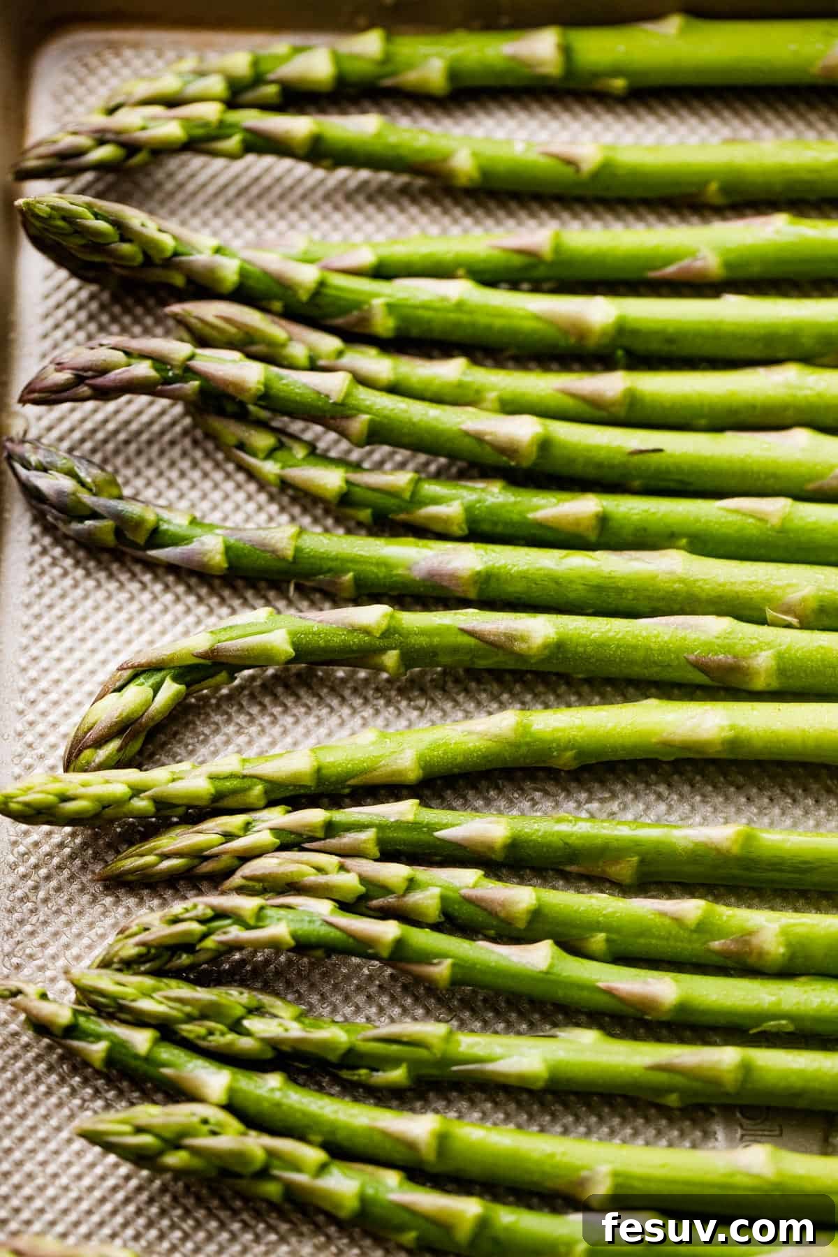 Raw asparagus spears arranged on a baking sheet, showcasing their freshness.