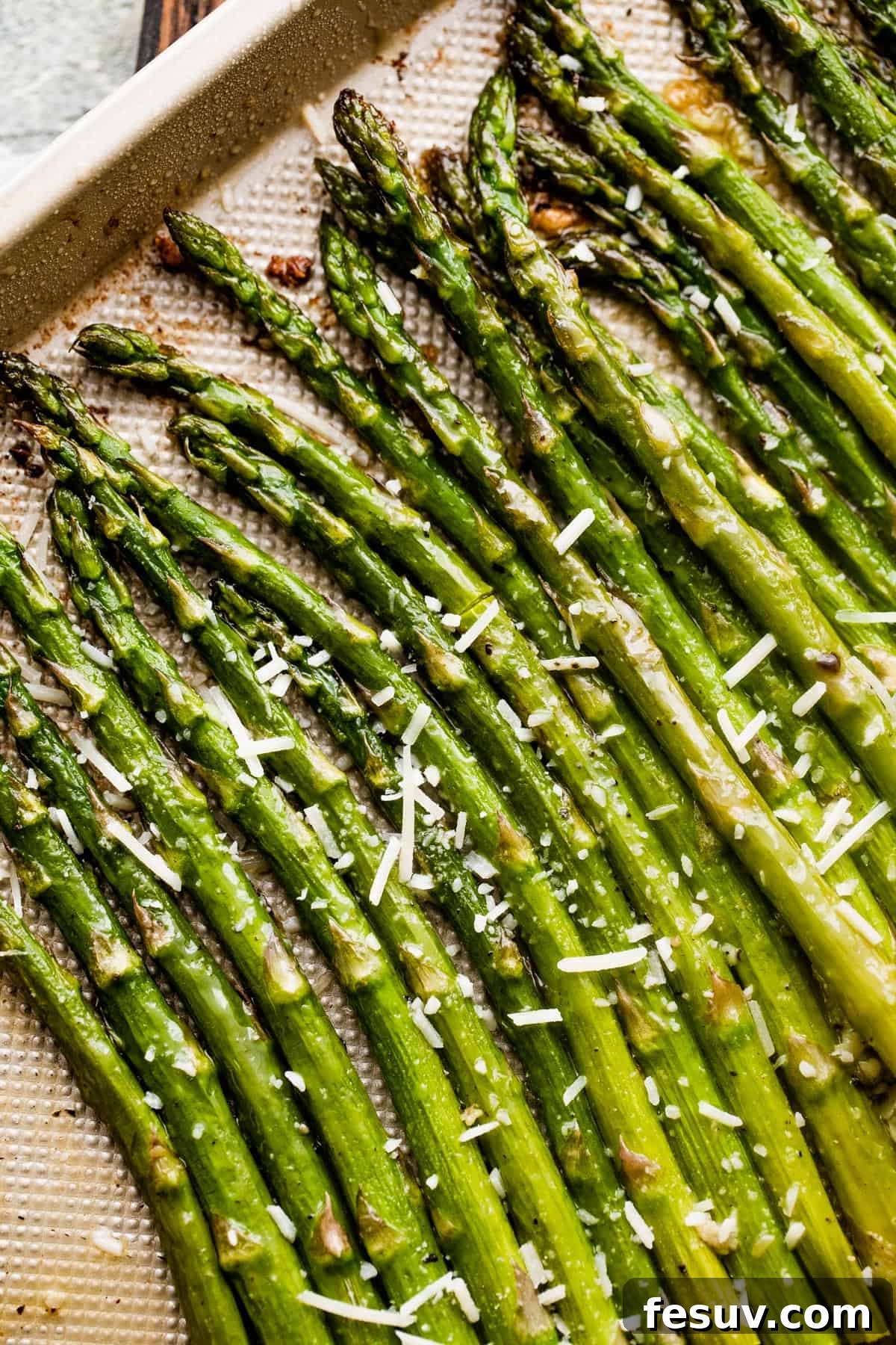 Parmesan-topped roasted asparagus spears arranged on a gold-colored baking sheet, ready to be served.