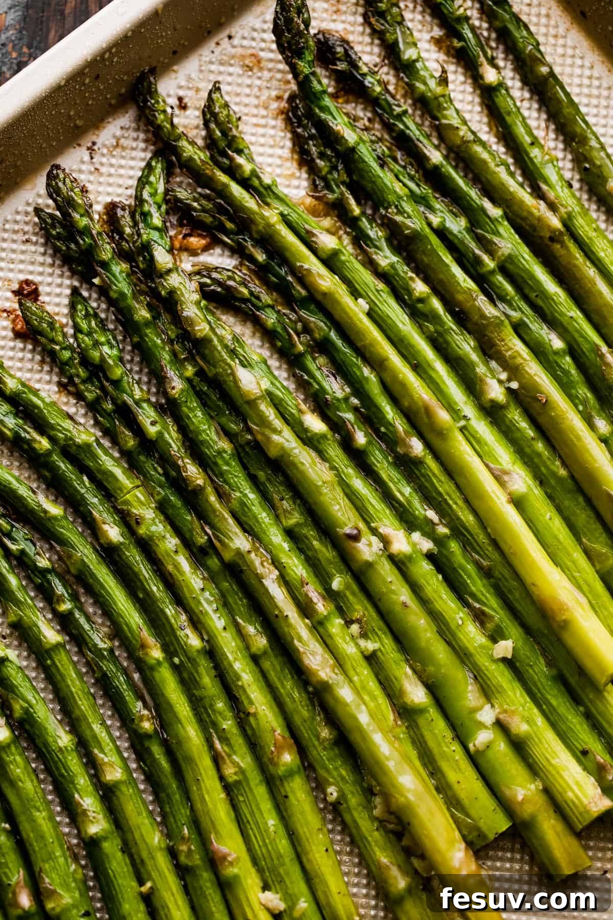 Close-up shot of perfectly roasted asparagus spears on a gold-colored baking sheet, showing their texture and slight char.