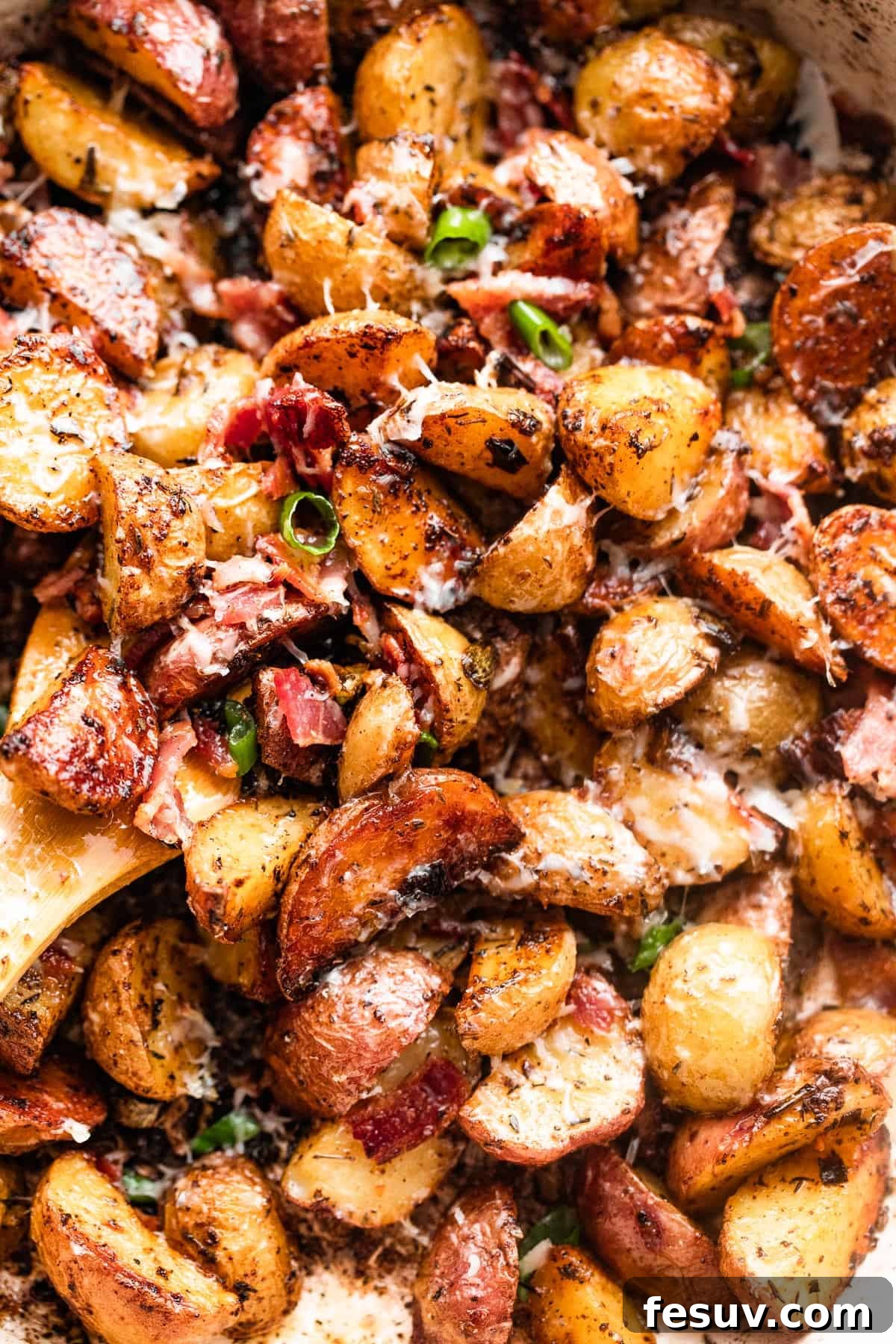 Golden Roasted Potatoes with Bacon and Cheese 3 close up shot of a wooden spoon stirring through roasted potatoes with bacon and cheese.