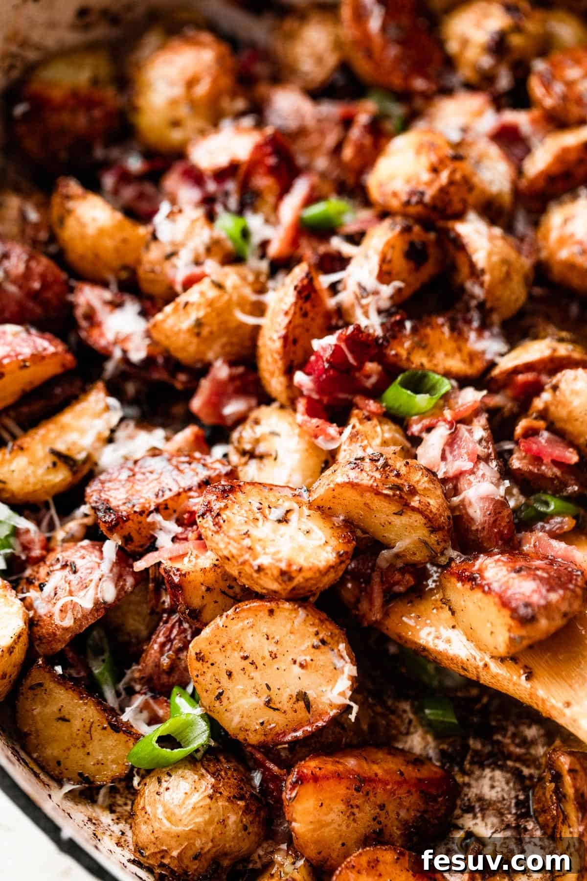 Golden Roasted Potatoes with Bacon and Cheese 6 close up shot of a wooden spoon stirring through roasted potatoes with bacon and cheese.