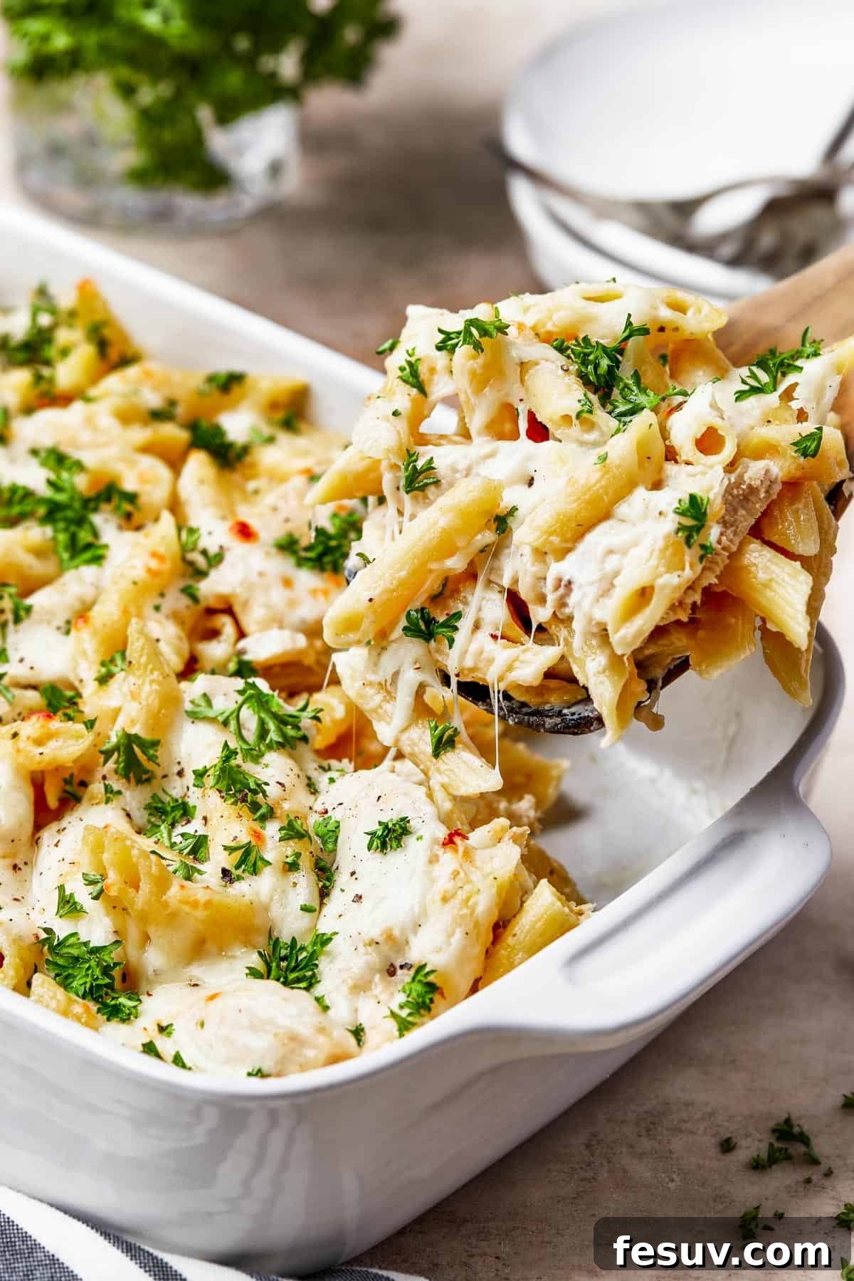 Chicken alfredo pasta being scooped out of a casserole dish.