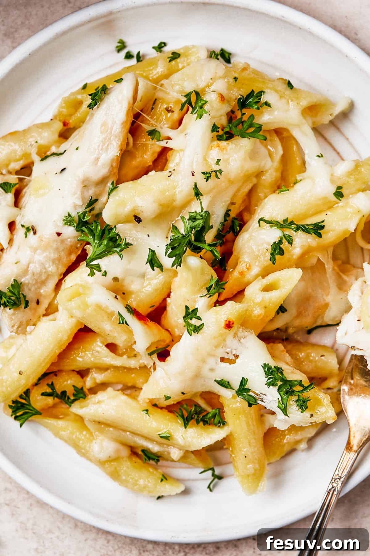 Overhead shot of chicken alfredo pasta bake on a plate, with a fork. The casserole dish is nearby on the table.