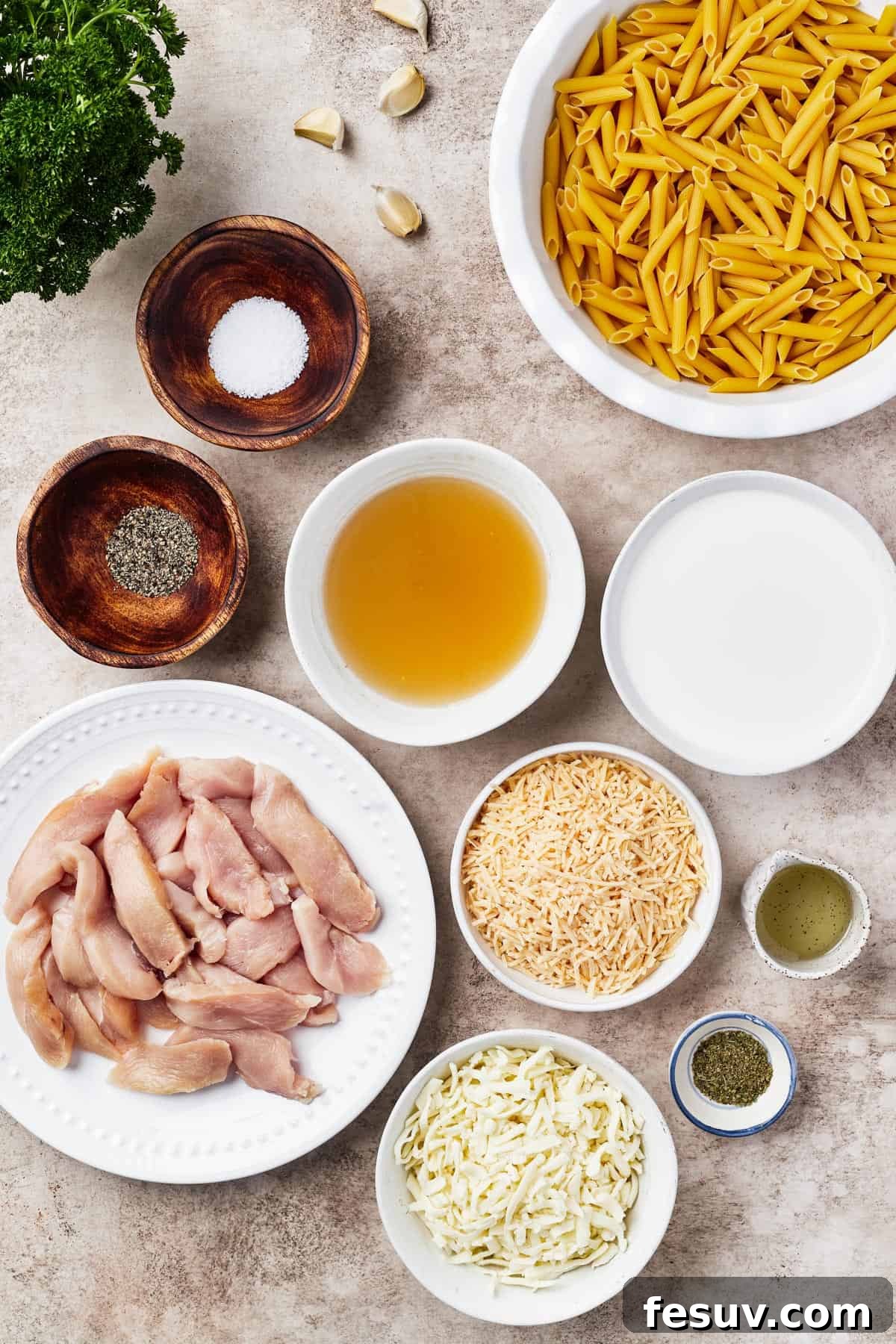 From top left: Parsley, garlic, penne pasta, salt and pepper, chicken broth, heavy cream, raw chicken, parmesan cheese, oil, mozzarella cheese, herbs.