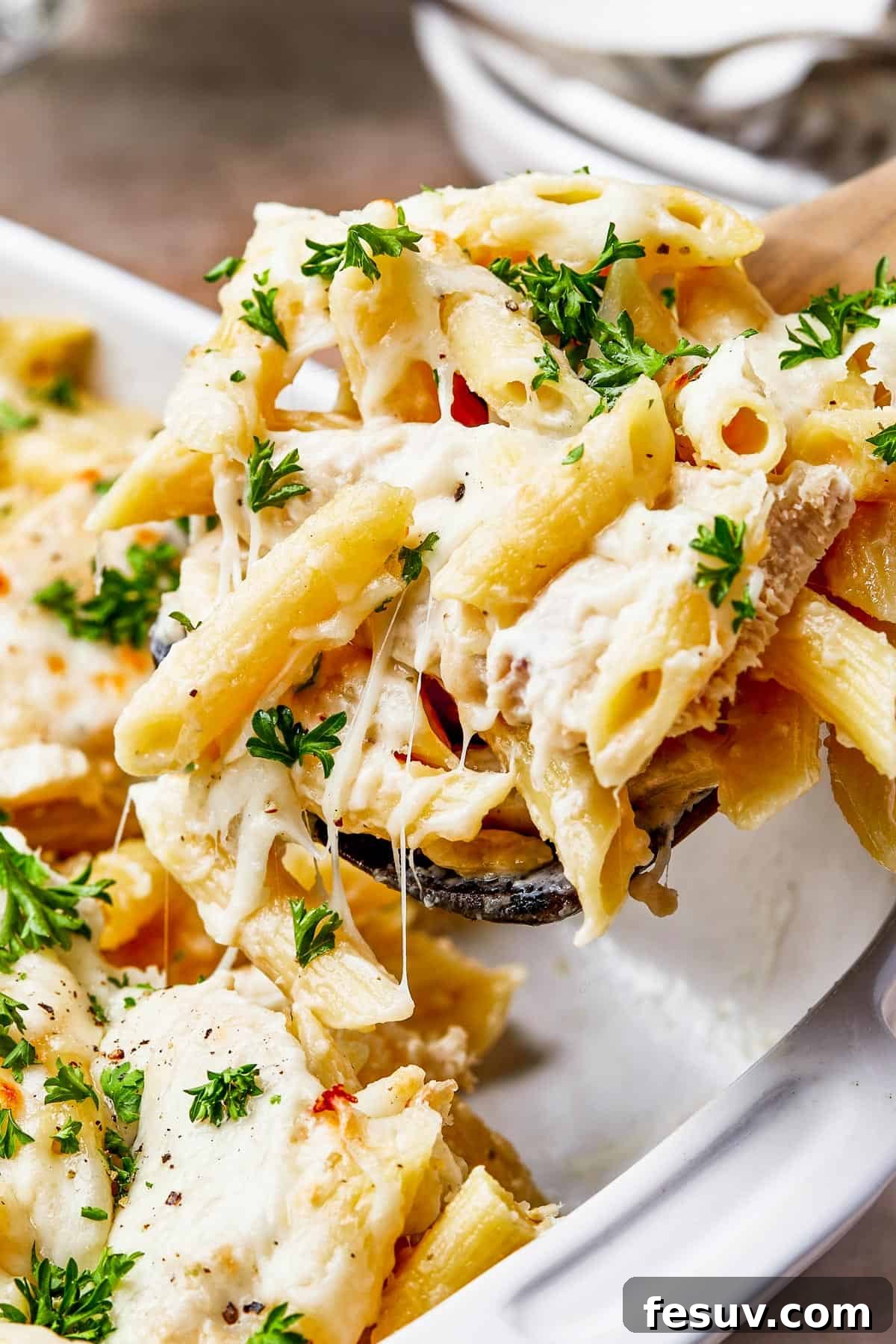 close up shot of chicken alfredo pasta being scooped out of a casserole dish.