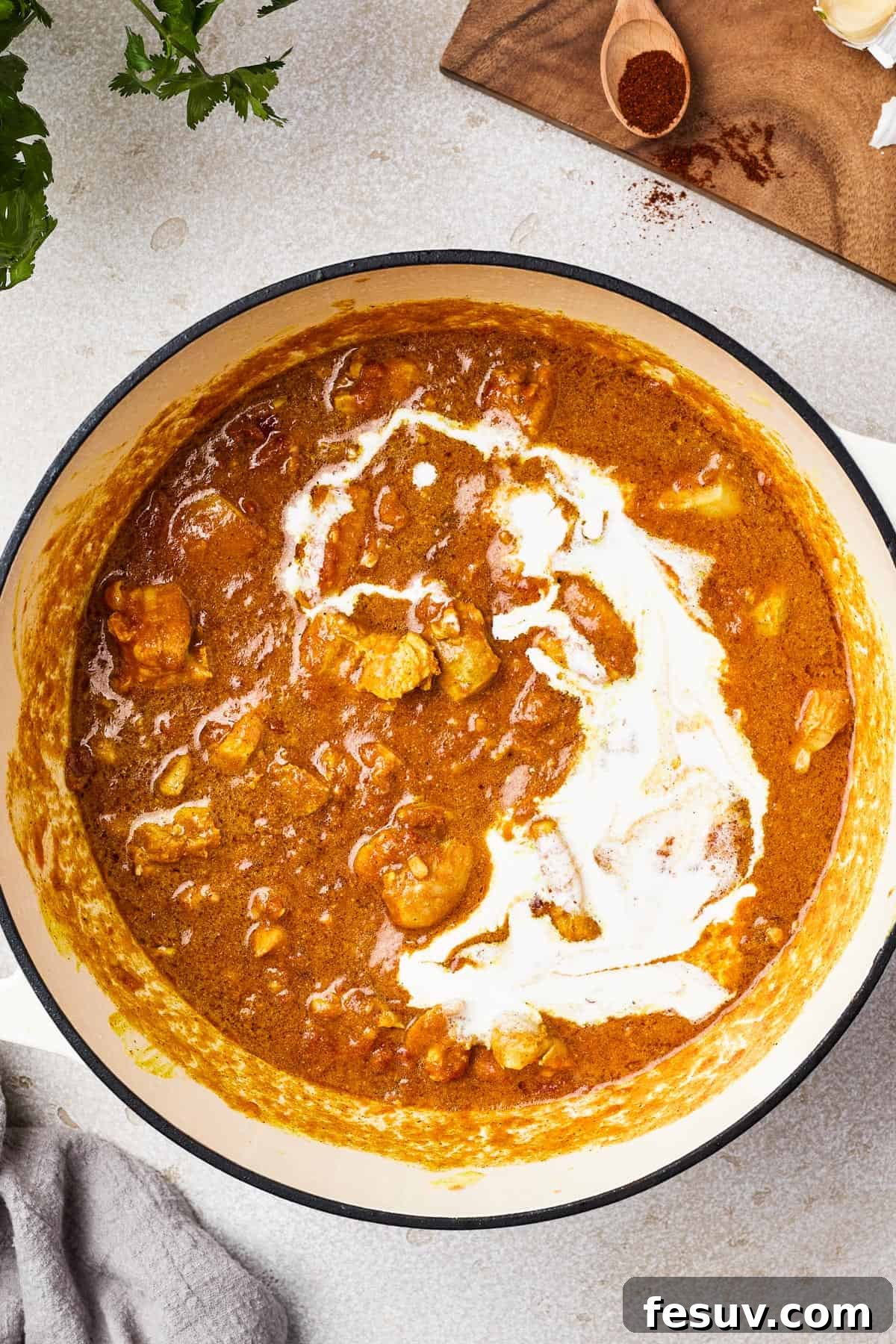 A heavy pot with chicken in a tomato sauce. Cream has been poured over the sauce.
